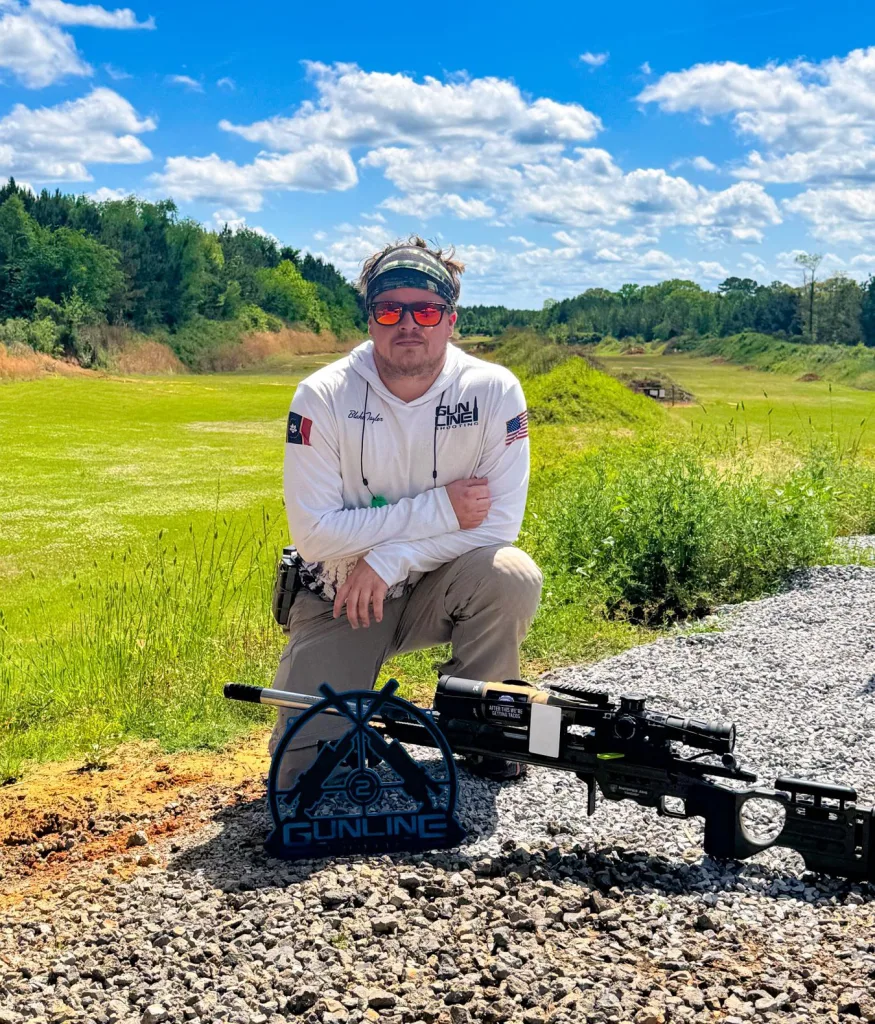 Blake Taylor kneeling beside his rifle and a Gunline Shooting trophy at the range